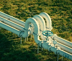 Conduite industrielle équipée de vannes et de raccords, traversant un espace extérieur recouvert d'herbe.