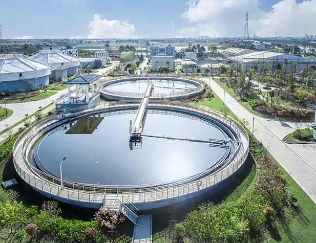 Deux grands bassins circulaires de traitement de l'eau, remplis d'eau bleue et entourés d'herbe verte