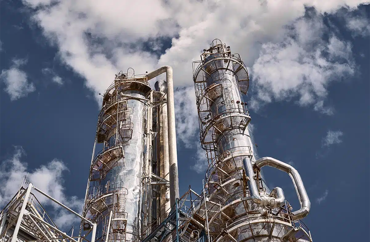 Two tall, shiny industrial towers with complex piping stand against a blue sky with scattered clouds.