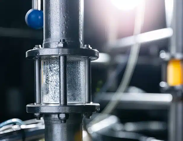 Gros plan sur un tuyau industriel dans lequel s'écoule un liquide transparent, maintenu par des colliers de serrage
