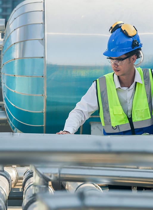 Man in bright yellow vest and blue hard hat inspecs a metal pipe