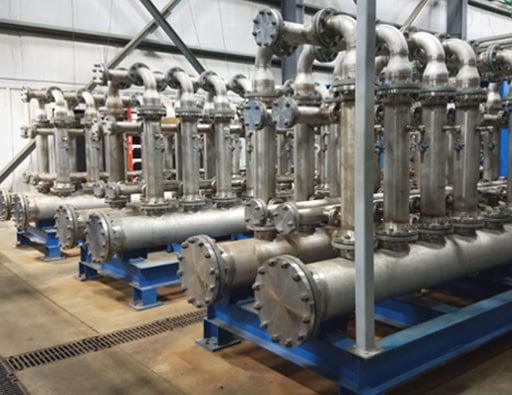 Réseau de tuyauterie industrielle en acier inoxydable et système de filtration installés dans une usine de transformation.