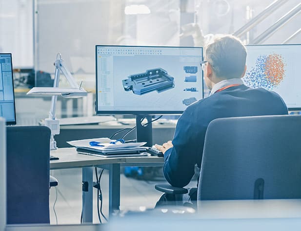 Man sitting at desk with monitors surrounding him and monitor has machinery on it