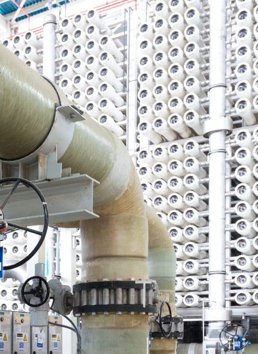 Rows of cylindrical filters line the wall of an industrial facility, with large pipes and valves in the foreground.