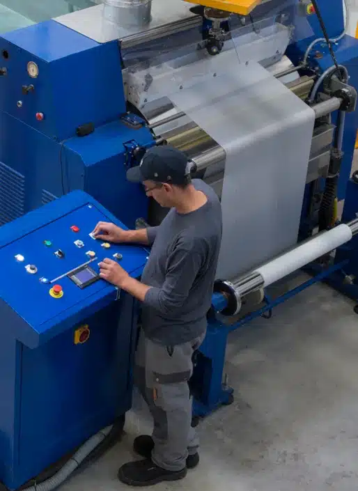 Man in all grey outfit and grey baseball cap pressing buttons on a blue machine.