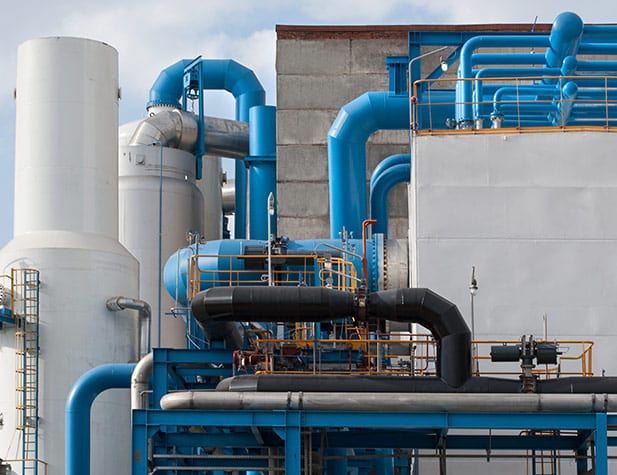 Industrial plant with blue and black pipes, large white tanks, and grey walls.