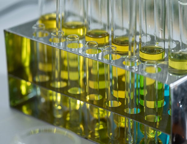 Test tubes with yellow liquid are arranged in a silver rack, reflecting light and casting a mirrored glow.