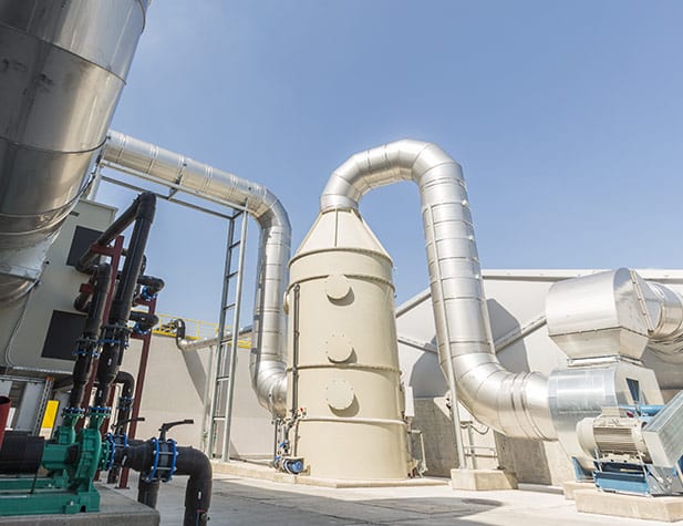 Industrial setting with large metal pipes and tanks against a clear blue sky.