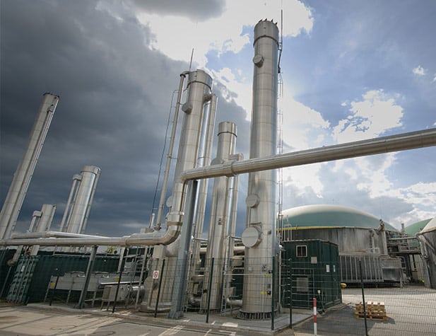 Industrial facility with tall stainless steel pipes under a dramatic sky.