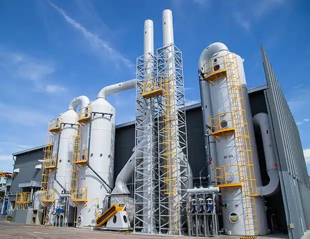 Industrial facility with tall, cylindrical structures and interconnected pipes against a clear blue sky.