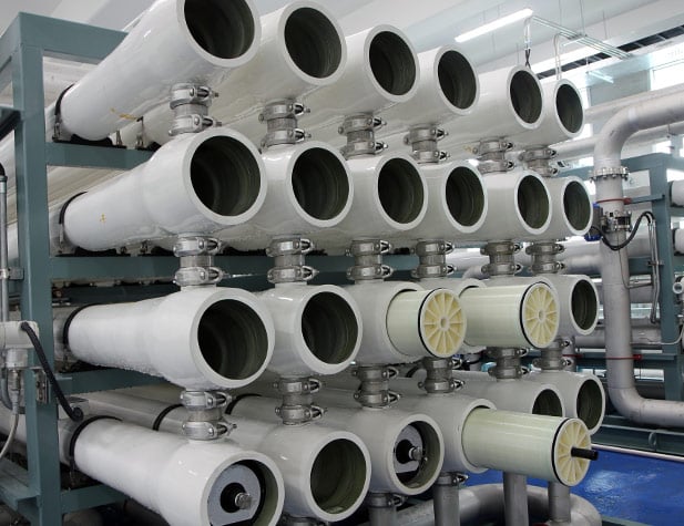 Des rangées de gros tuyaux blancs disposés dans une station de traitement des eaux industrielle.