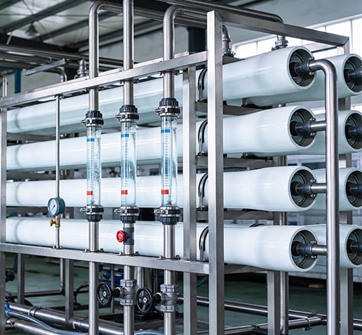 A modern industrial water filtration system with multiple white cylindrical filters is interconnected by metal pipes.