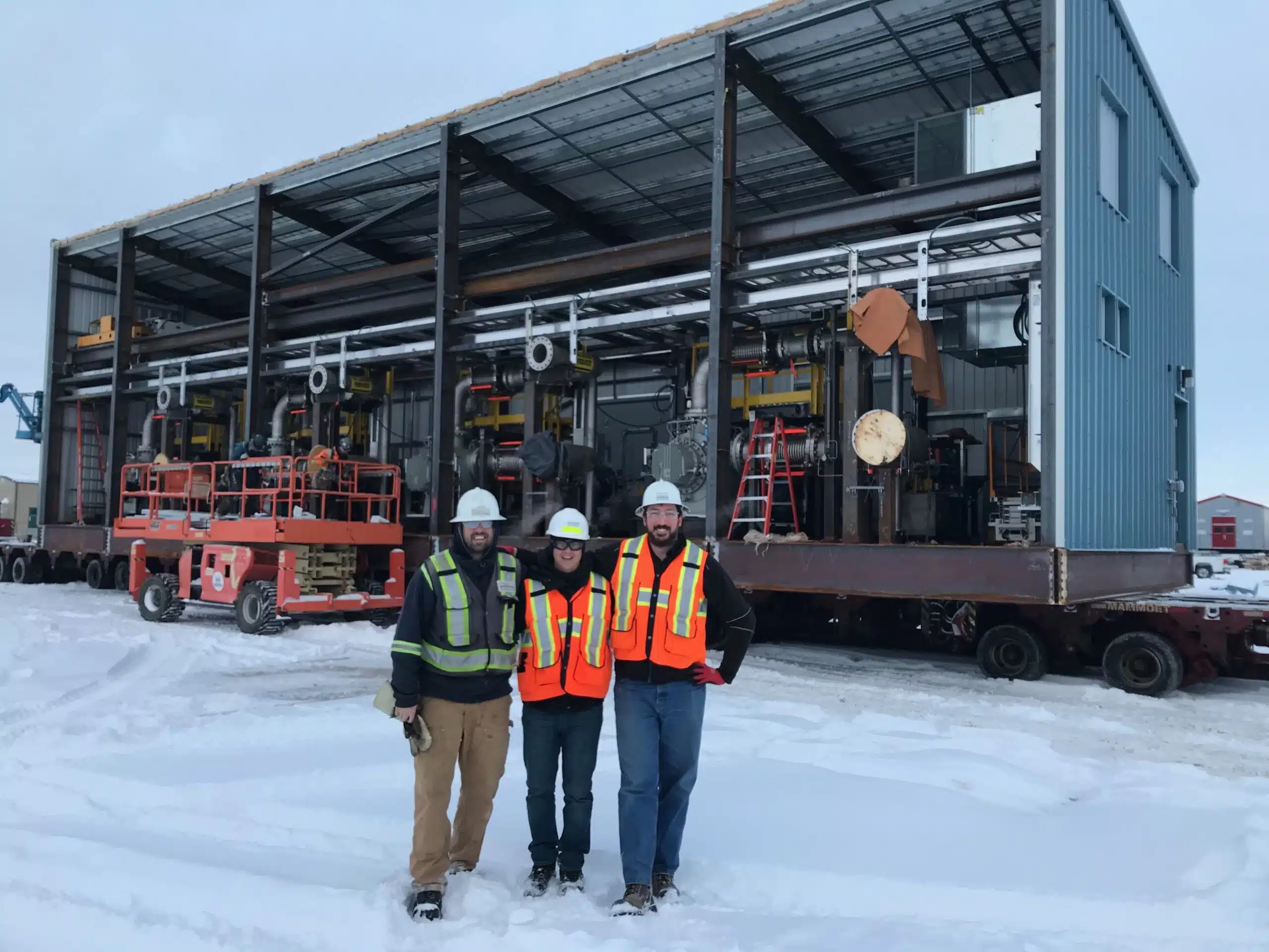 people in a snow covered field with large modular water treatment equipment in the background
