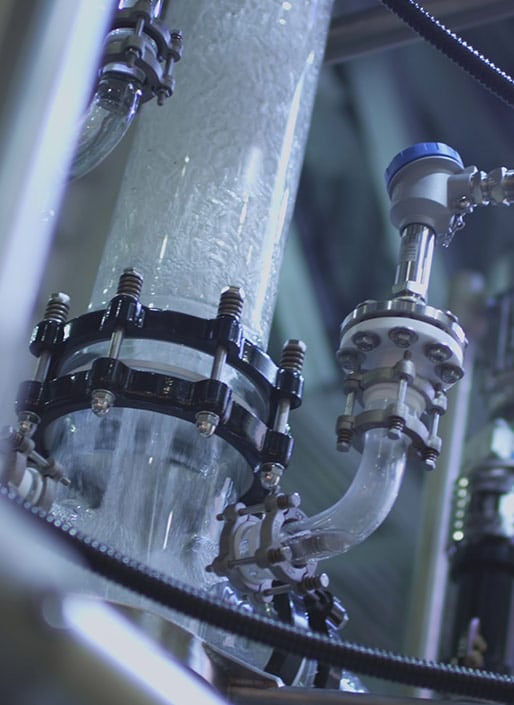 Close-up of an industrial pipe with flowing transparent liquid, secured by clamps and surrounded by metal valves.