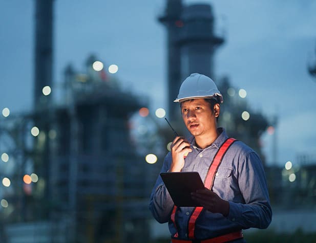 Un homme portant un casque de chantier blanc, tenant une tablette et parlant dans un talkie-walkie