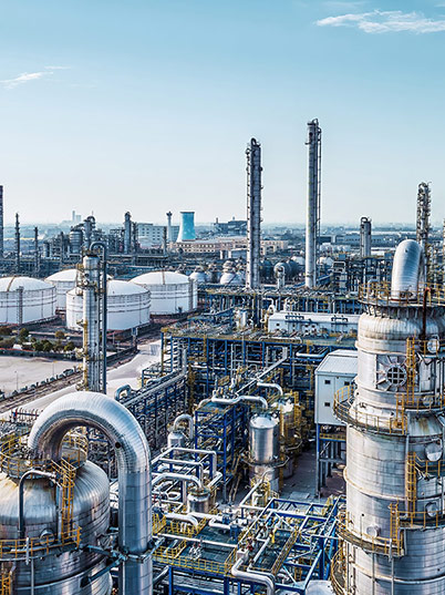 A sprawling industrial refinery with tall towers, pipes, and storage tanks under a clear blue sky.