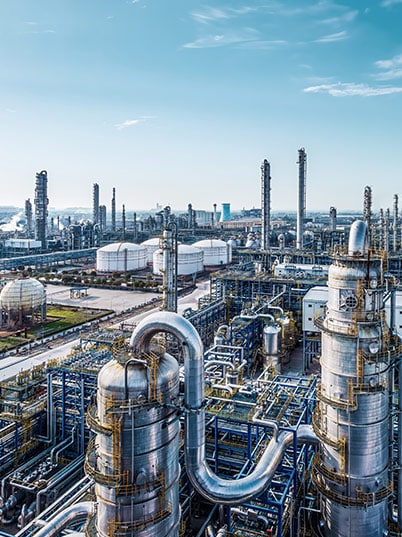 A sprawling industrial refinery with tall towers, pipes, and storage tanks under a clear blue sky.