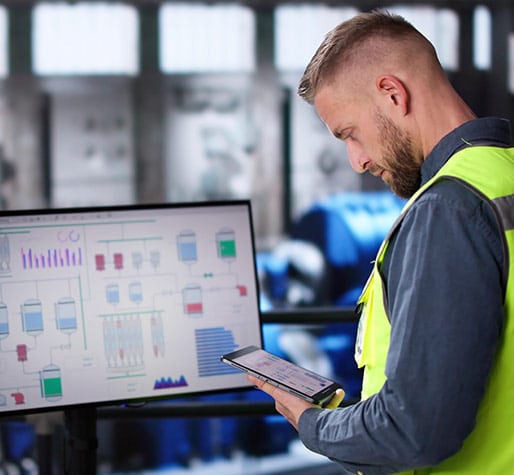 Man in reflective vest looking at tablet and computer monitor.