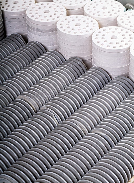 Stacks of white, round ceramic plates with small holes, in rows.