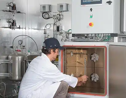 Un homme vêtu d'une blouse blanche de laboratoire et d'une casquette de baseball, en train de travailler sur un boîtier métallique